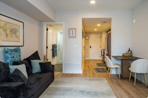 A modern living room with a sofa, a dining area with a table and chairs, and a kitchen with a refrigerator. - Stylish Fishtown 1BR - Prime Location (Philadelphia)