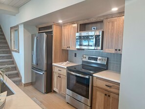 A modern kitchen with stainless steel appliances, wooden cabinetry, and a tiled backsplash. - Summers on Detroit Lake (Detroit Lakes)