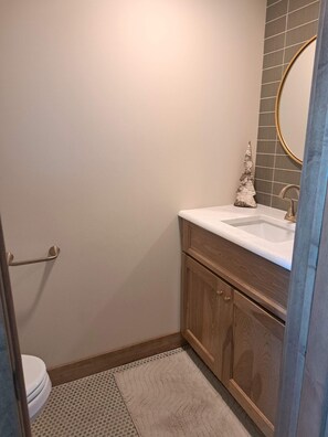 A bathroom with a toilet, a sink with a mirror, and a wooden cabinet. - Summers on Detroit Lake (Detroit Lakes)
