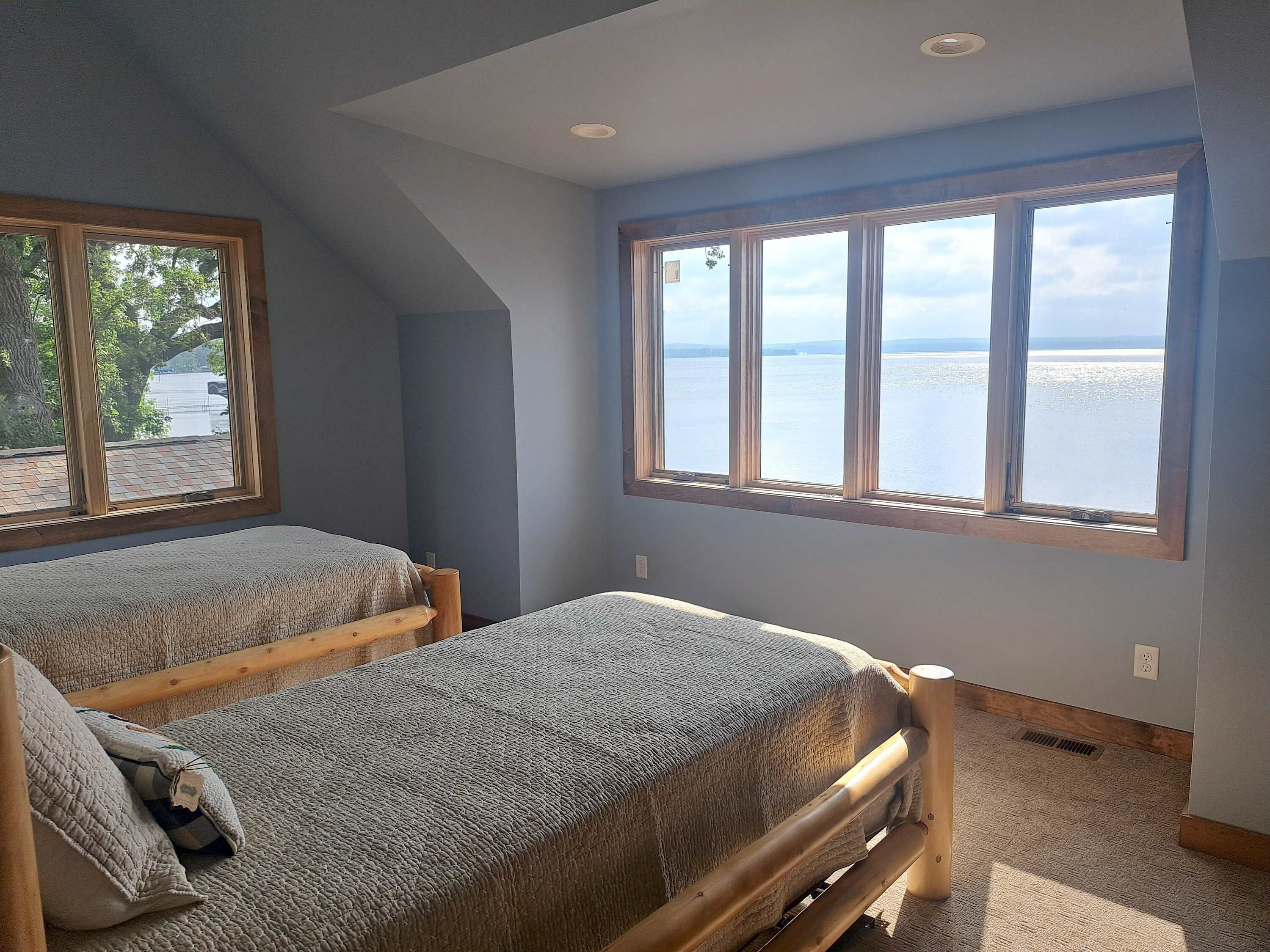 Ein Schlafzimmer mit zwei Betten, einem großen Fenster mit Blick auf ein Gewässer und einer geneigten Decke.