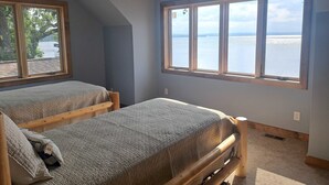 Ett sovrum med två sängar, ett stort fönster med utsikt över en sjö eller ett annat vattendrag och ett sluttande tak.