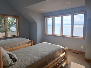 Ein Schlafzimmer mit zwei Betten, einem großen Fenster mit Blick auf ein Gewässer und einer geneigten Decke.
