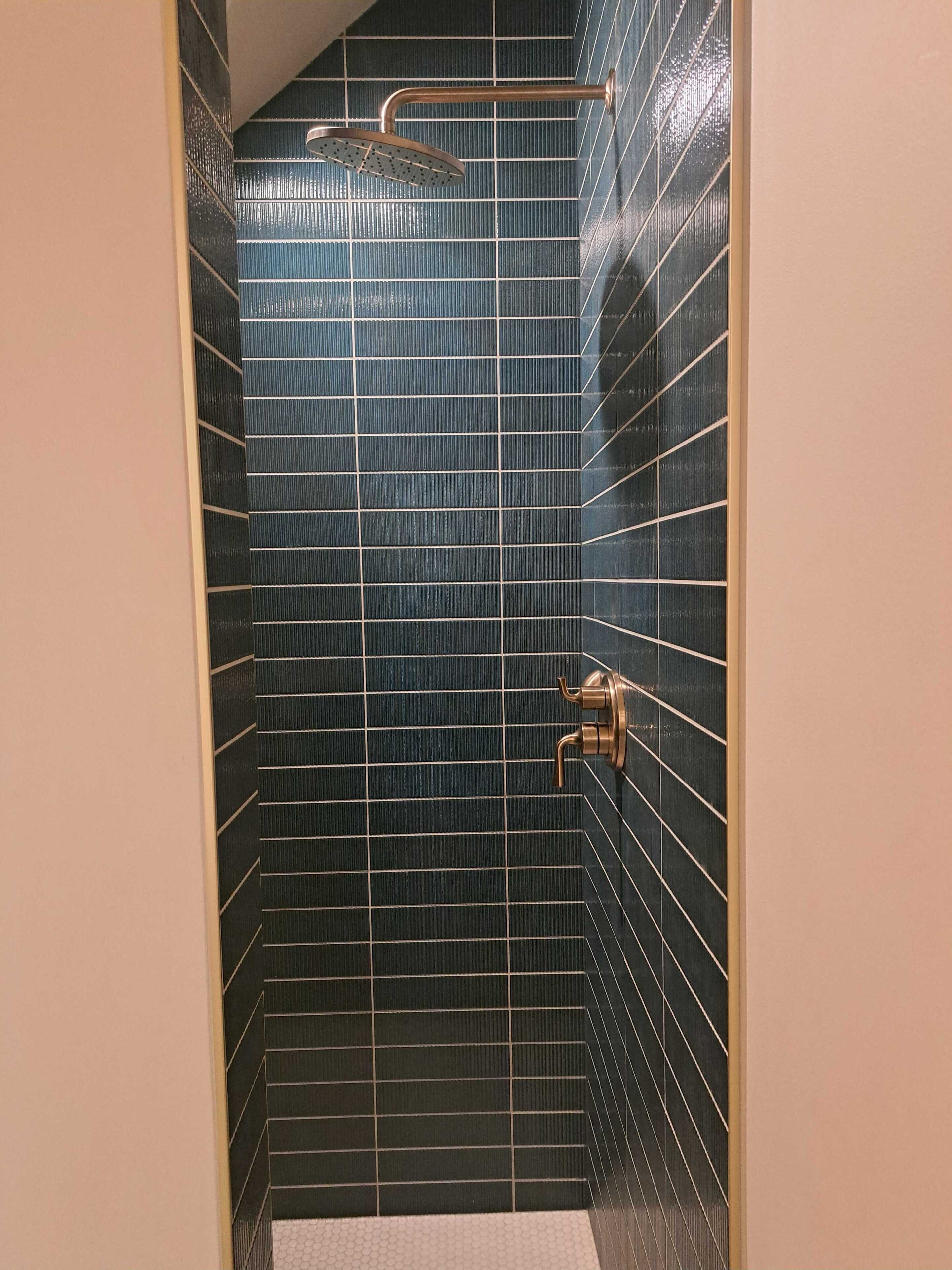 Ein Badezimmer mit dunkelblauen Fliesen, einer Duschbrause und einem Handtuchhalter.