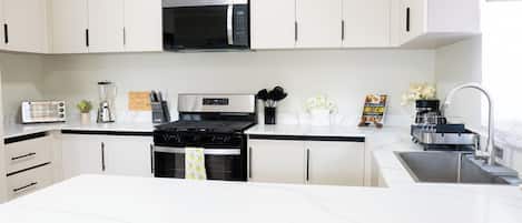 A modern kitchen with white cabinetry, a built-in microwave, a stove, a toaster, and a coffee maker.