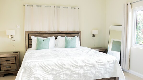 A hotel room with a bed, bedside tables, a nightstand, a bedside lamp, and a window with curtains. - Beautiful 3-bedroom house with AC in charming Ocho Rios (Ocho Rios)