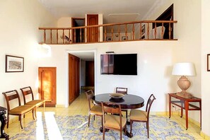A dining area with a round table, chairs, a television, and a lamp. - Historic Via Giulia Loft by Flatinrome (ROMA)