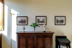 A room with a wooden cabinet, a vase with flowers, and three framed pictures on the wall. - Historic Via Giulia Loft by Flatinrome (ROMA)