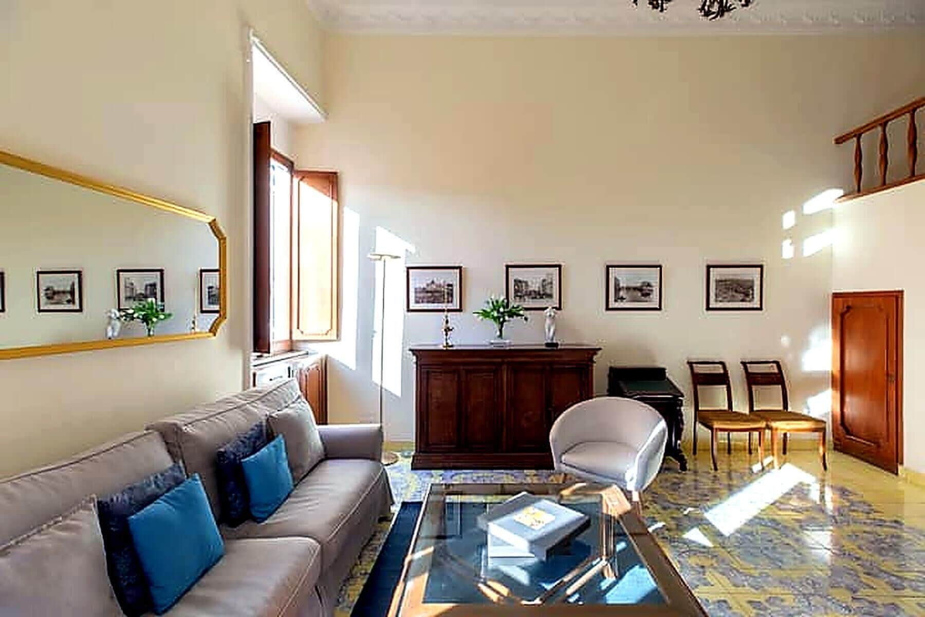 A living room with a sofa, a glass coffee table, a desk with a chair, and framed pictures on the wall.
