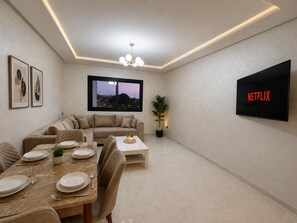 A modern living room with a sofa, dining table, and a TV displaying 'NETFLIX'. - Fabulous 3-bedroom, 2 bathroom apartment with free parking in vibrant Tanger (Tanger)