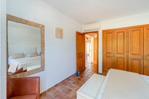 Un dormitorio con cama, una silla, armario, espejo y una puerta que da a otra habitación.
