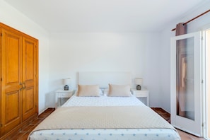 A bedroom with a bed, two bedside tables, a wardrobe, and a sliding glass door. - Casa Massieu - Relax steps from the beach (Ciutadella de Menorca)