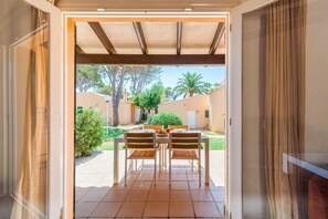 An open doorway leading to a patio with a table and chairs, surrounded by greenery and a clear sky. - Casa Massieu - Relax steps from the beach (Ciutadella de Menorca)