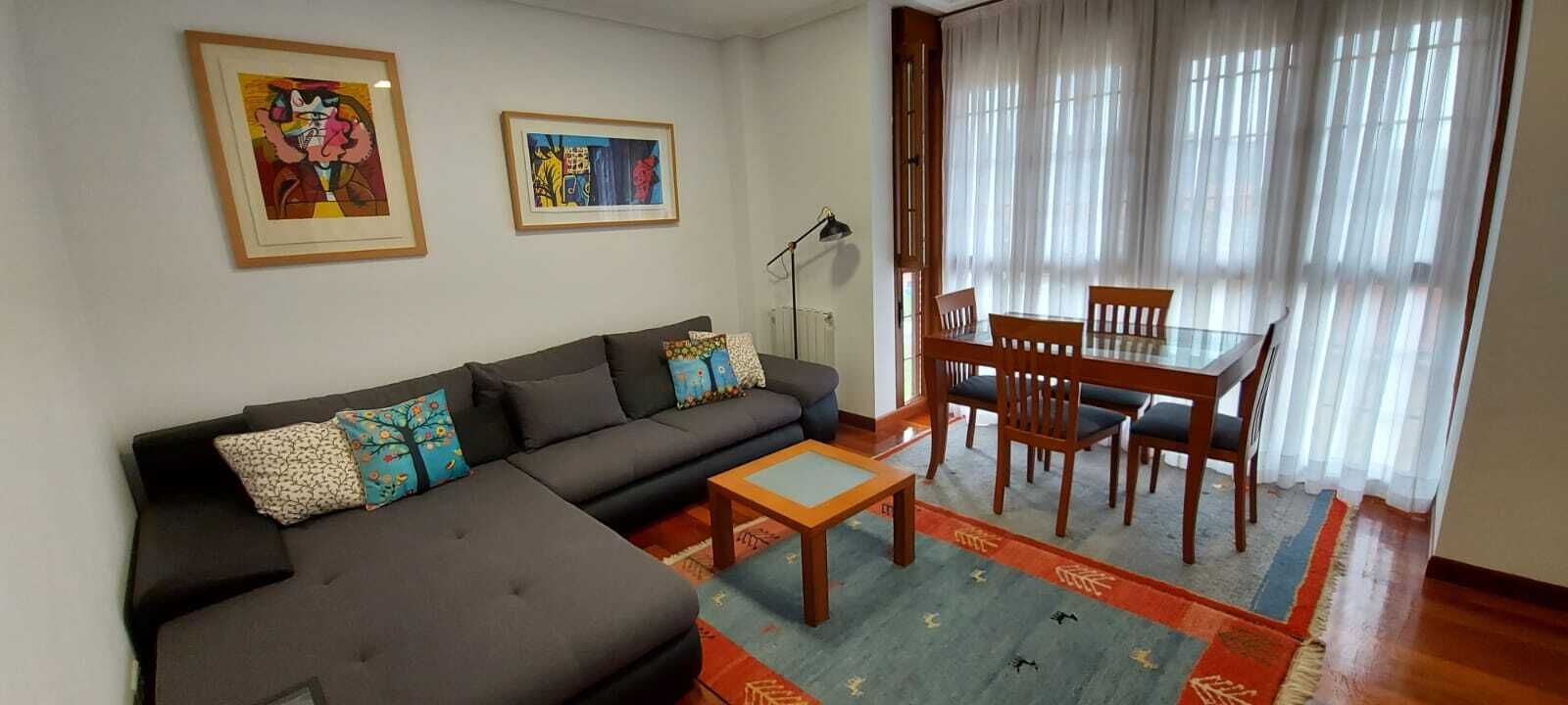 Una sala de estar con sofá, una mesa de centro, una mesa de comedor con sillas y dos obras de arte enmarcadas en la pared.