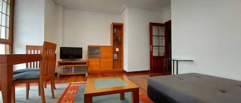 Un soggiorno con un divano, una televisione, un mobile in legno e una porta con pannelli di vetro.