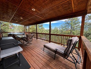 A covered outdoor deck with a hot tub, a table, and chairs. - Peaceful Redwood Retreat Cabin with Hot Tub & Incredible Forest Views (Ruidoso)