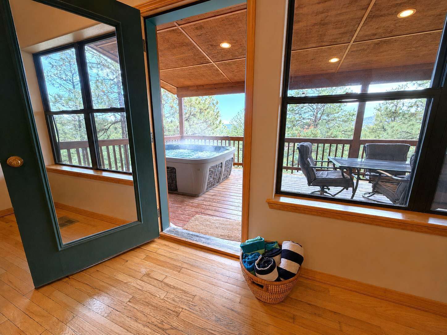 A room with a wooden floor, a large window, and a view of an outdoor deck with a hot tub and seating area.