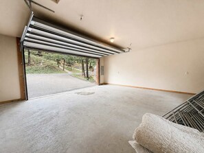 A spacious room with a large garage door, a concrete floor, and a view of a road and greenery outside. - Peaceful Redwood Retreat Cabin with Hot Tub & Incredible Forest Views (Ruidoso)