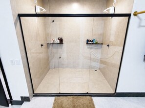A modern shower enclosure with a glass door, a towel rack, and a shelf with toiletries.