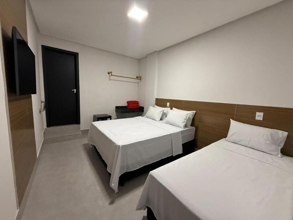 A hotel room with two beds, a flat-screen TV, a small table, and a door.