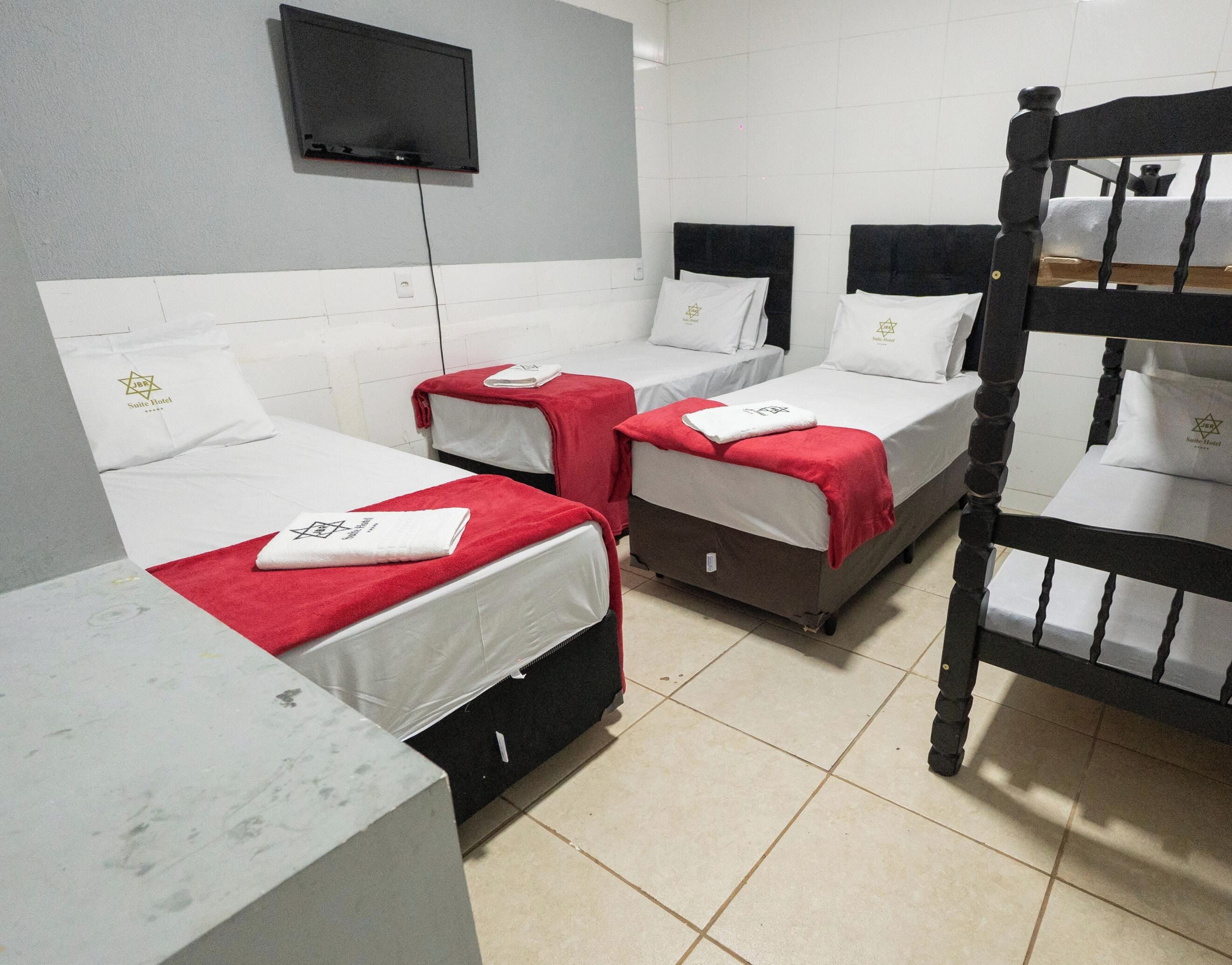 Ein Hotelzimmer mit drei Betten, jeweils mit roter Decke und weißen Kissen, einem flachbildfernseher an der Wand und einem hölzernen Etagenbett.