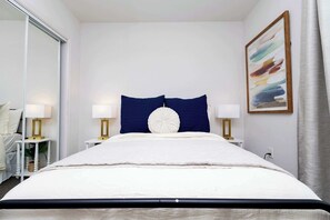 A hotel room with a large bed, two bedside tables with lamps, a mirror, a painting, and a curtain.