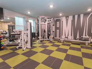 Ein Fitnessraum mit unterschiedlichen Trainingsgeräten, einem Schachbrettmuster-Boden und einer Wand mit großen Lettern.