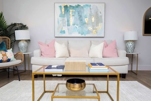 Ein Wohnzimmer mit einem weißen Sofa, einem Glastisch und zwei Beistelltischen mit Lampen.
