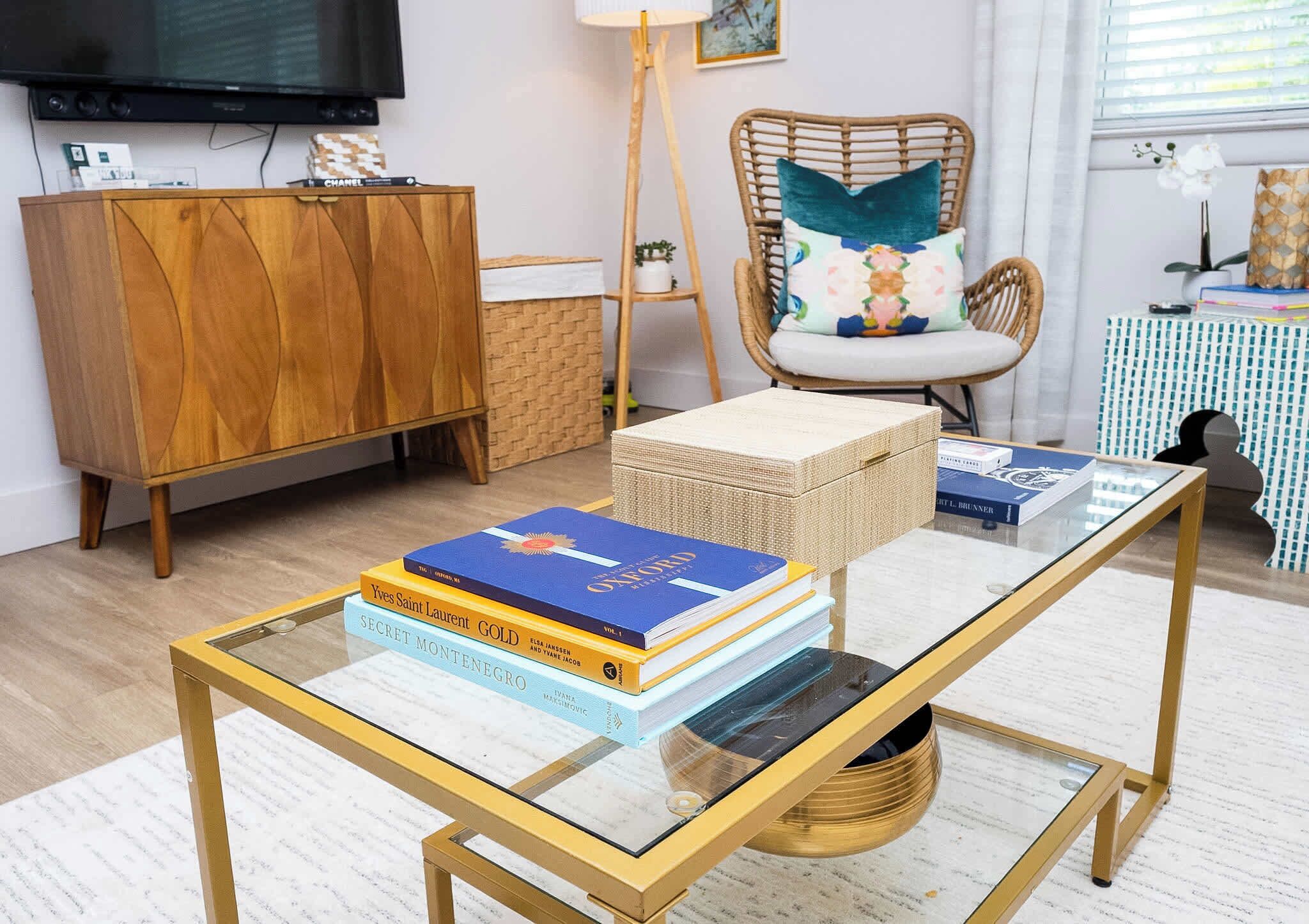 A modern living room with a glass-top coffee table, a wooden cabinet, a wicker chair, and a television mounted on the wall.