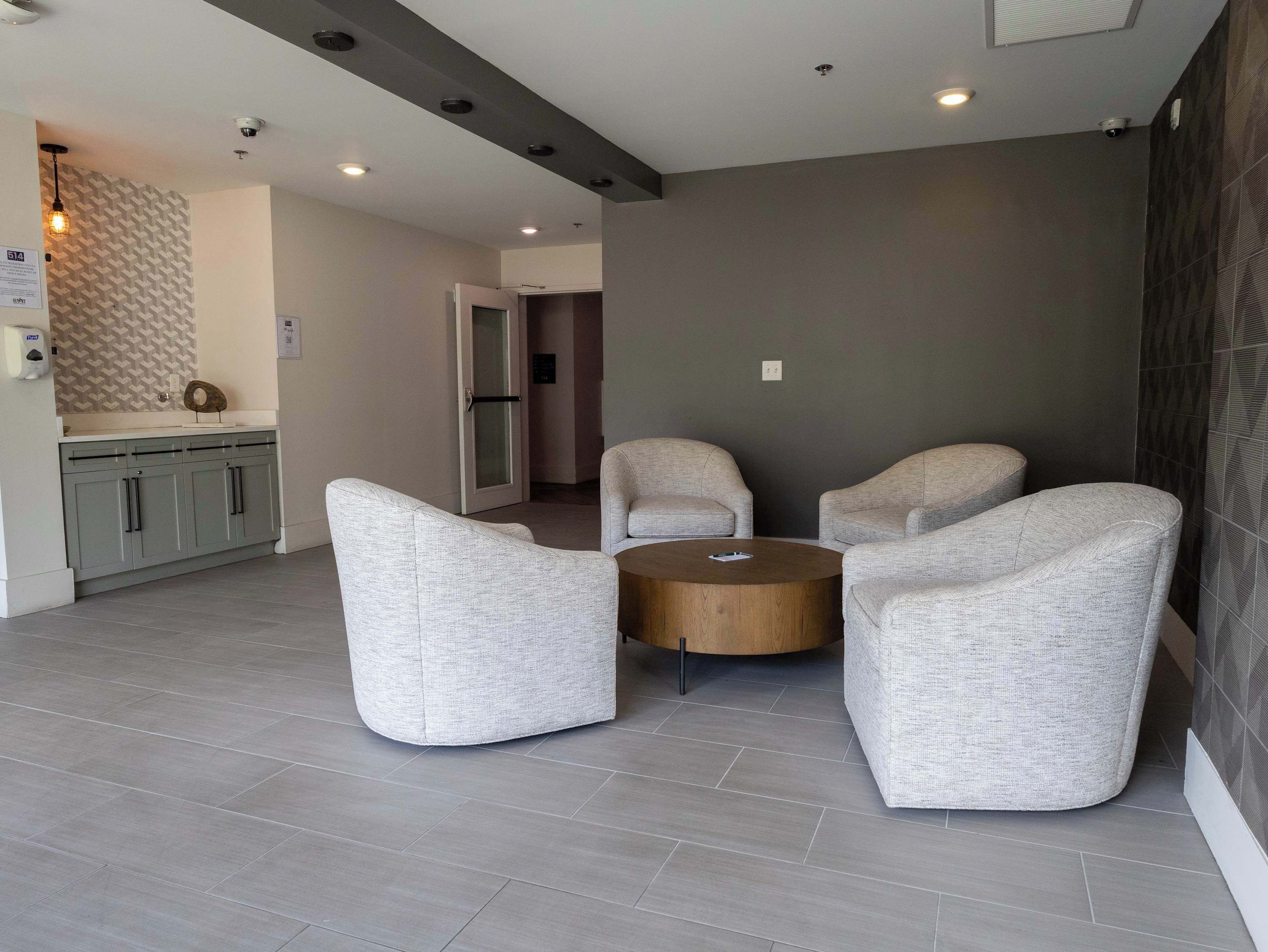 A modern living room with grey sofas, a wooden coffee table, and a kitchen area with grey cabinets.