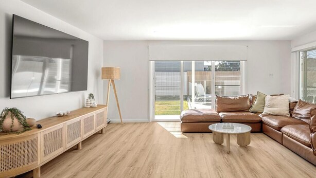 Een moderne woonkamer met een grote flatscreen-tv, een houten salontafel, een bruine leren bank en een glazen deur naar een buitenruimte.