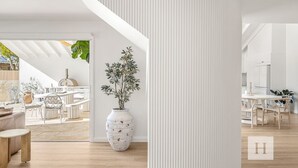 Een modern interieur met een grote witte vaas, houten vloeren en een eethoek met witte meubels.