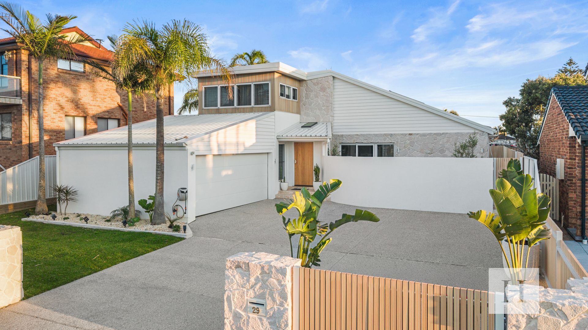 A modern residential property with a spacious driveway, a well-maintained lawn, and a variety of tropical plants.