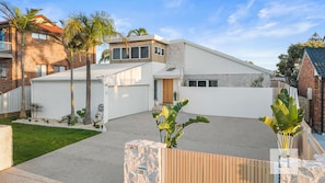 A modern residential property with a spacious driveway, a well-maintained lawn, and a variety of tropical plants.