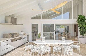 A modern kitchen with a built-in grill, white cabinetry, and a dining area with a round table and wave-patterned chairs.