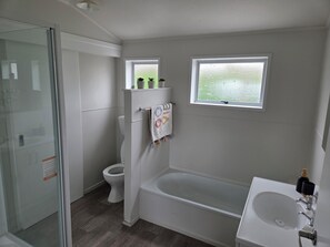 Un baño con cabina de ducha de vidrio, inodoro, bañera y ventana con vistas al exterior.