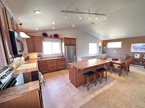 A modern kitchen with wooden cabinets, a stainless steel refrigerator, and a large island with bar stools. - Black Dog Inn - Minutes from The Gorge (Quincy)