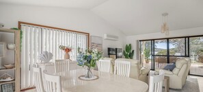 Un espacio habitable amplio con una mesa de comedor, sillas blancas, un sofá y un ventanal que ofrece vistas al exterior.