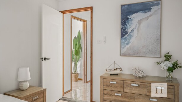 A room with a wooden cabinet, a white door, a wall-mounted painting, and a potted plant.