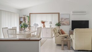 A modern living room with a dining area, featuring a sofa, chairs, a TV, and a fireplace.