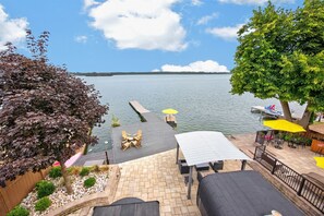 Eine Terrassensitzgelegenheit am Seeufer, eine Stegvorrichtung, die ins Wasser hineinreicht, und Blick auf den See und die entfernte Uferlinie.
