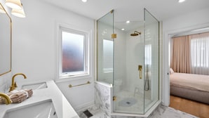 Une salle de bain moderne avec une douche à parois de verre, un lavabo blanc doté de robinetterie dorée et une fenêtre en verre dépoli.