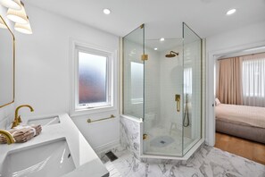Ein modernes Badezimmer mit einer gläsernen Dusche, einem weißen Waschbecken mit goldfarbenen Armaturen und einem Fenster mit Frostglas.