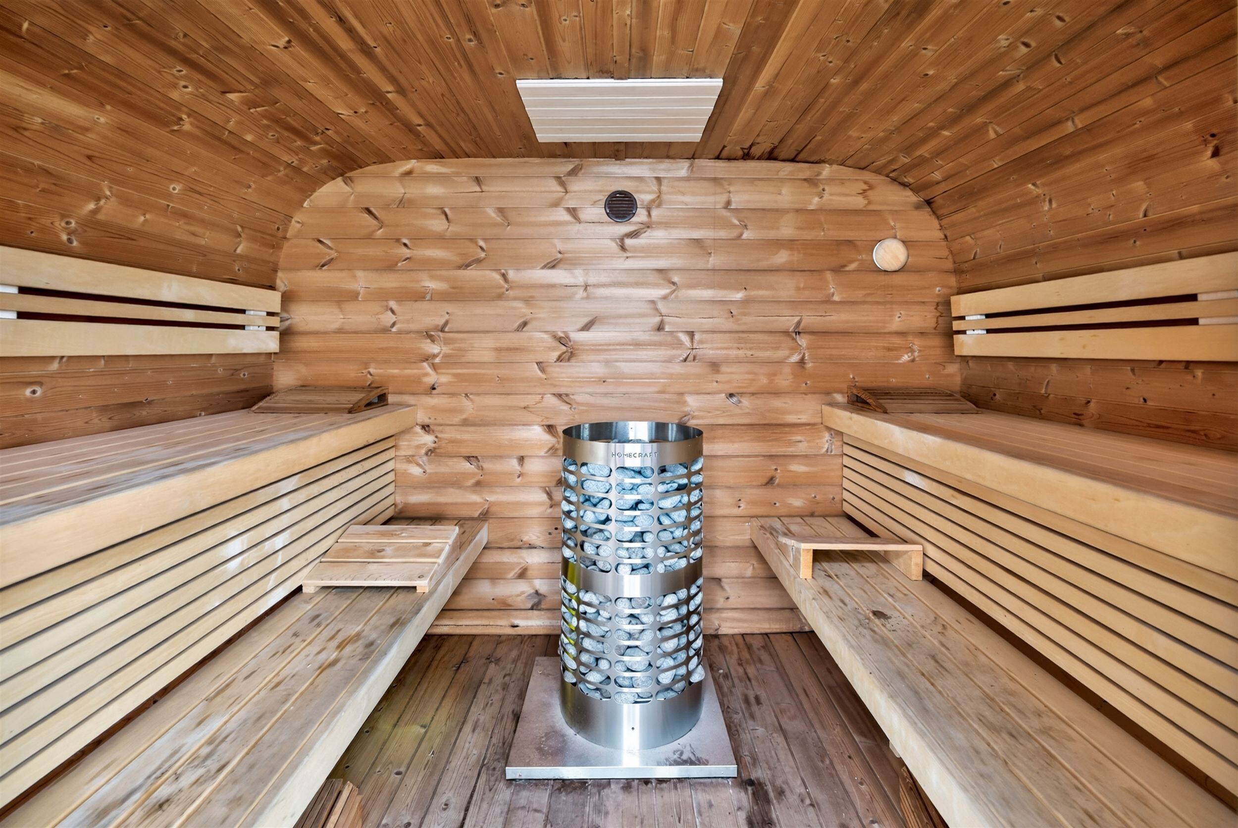 Eine Sauna mit Holzbänken, einem zentralen Dampfgenerator und einer geneigten Decke.