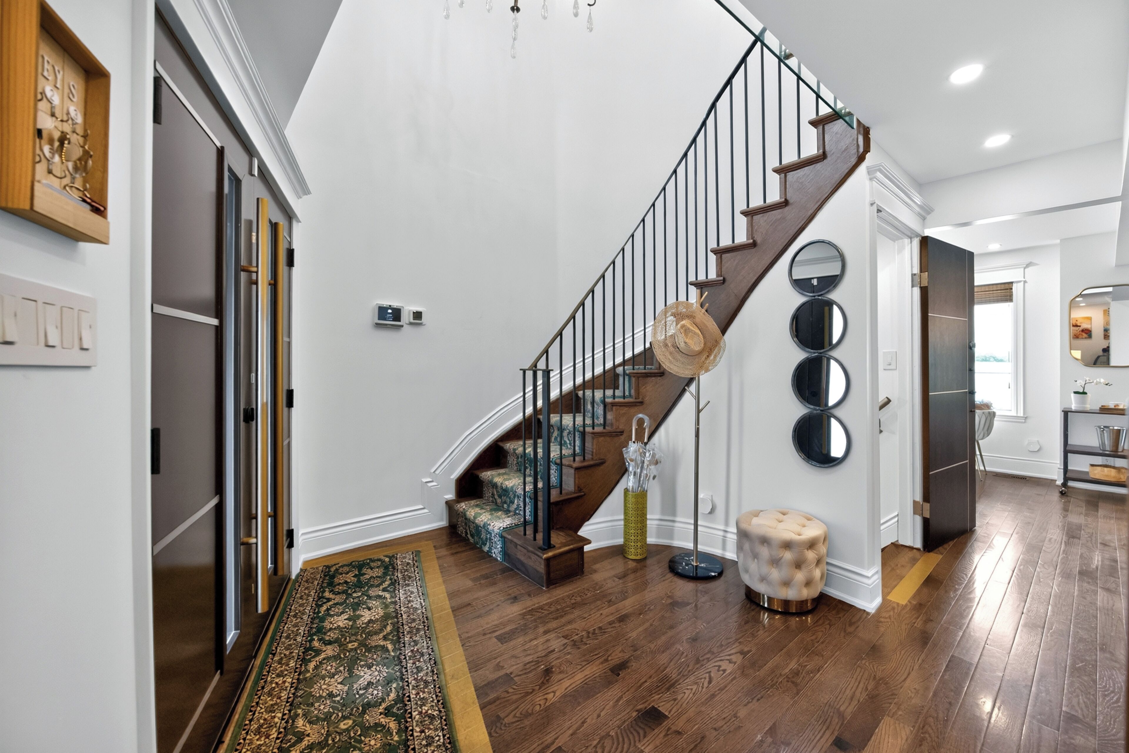 Una escalera con detalles de madera y barandillas de metal que conduce a una plataforma con un tapete estampado y un reposapiés redondo.