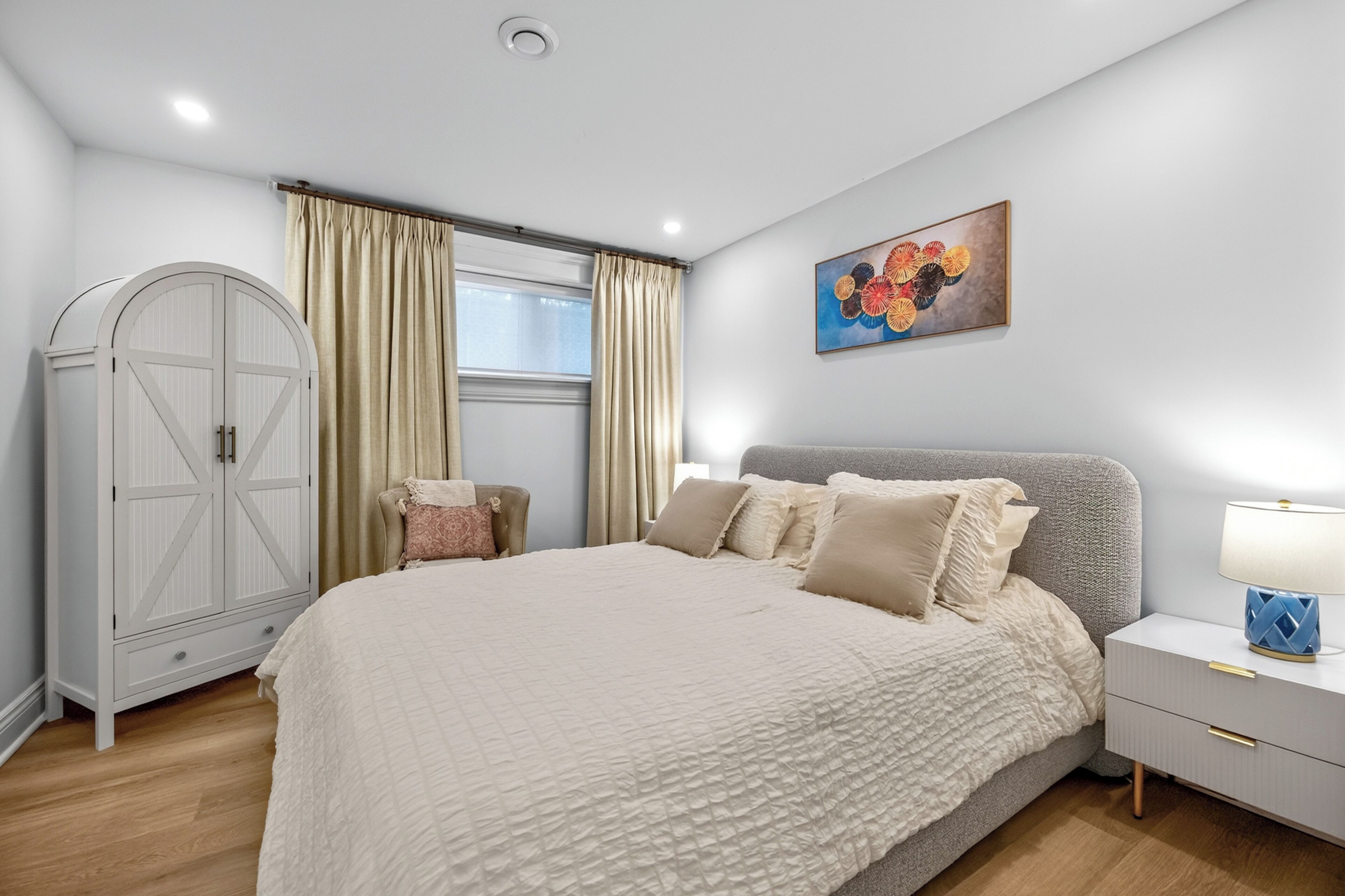 A bedroom with a bed, nightstand, lamp, wardrobe, and a window with curtains.