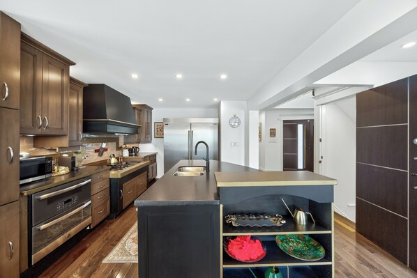 A modern kitchen with dark wood cabinets, stainless steel appliances, and a central island with a sink.
