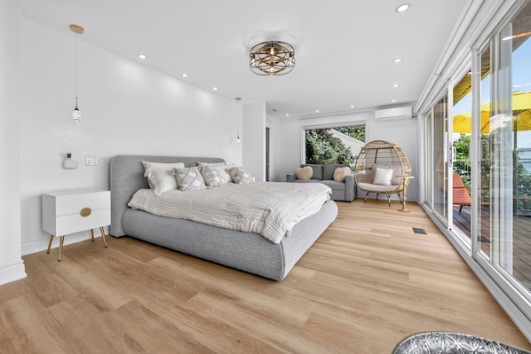 A modern bedroom with a large bed, bedside tables, a hanging light fixture, and a view of the outdoors.