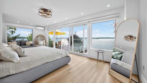Une chambre moderne avec un grand lit, un balcon donnant sur l’eau et un grand miroir.