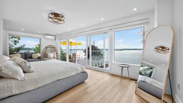 Une chambre moderne avec un grand lit, un balcon donnant sur l’eau et un grand miroir.