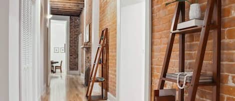 Hall | Interior Hallway Connecting Bedrooms with Exposed Beam Ceiling and Brick Wall | Third Floor of Building — Unit on One Level